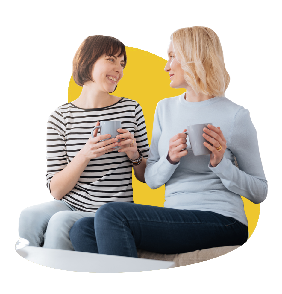 2 women sat next to each other, having a fun chat and tea time